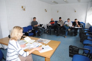 Zdjęcie kilkuosobowej grupy słuchaczy siedzących pod ścianami w sali wykładowej na krzesłach z pulpitami - na przedzie ujęcia widoczna za stołem wykładowcy koordyntorka przedsięwzięcia - Pani Marta Łomża
