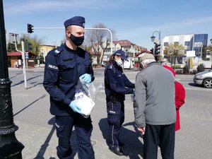 Policjanci dają na ulicy seniorom maseczki.