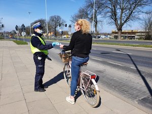 Policjant ruchu drogowego daje maseczkę rowerzystce.
