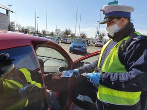 Policjant daje pasażerowi auta maseczkę.