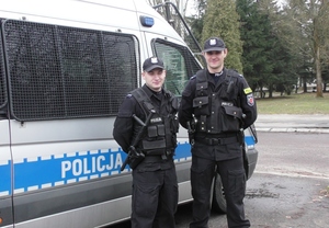 Dwóch policjantów stoi obok radiowozu.