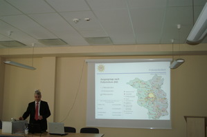 Zdjęcie niemieckiego prelegenta w trakcie wykładu obok ekranu z prezentacją