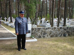 Zdjęcie funkcjonariusza w mundurze stojącego na tle grobów