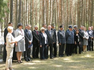 Zdjęcie części uczestników uroczystości (mundury policyjne i harcerskie) na polanie leśniej na tle drzew