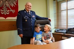 Gabinet komendanta. Inspektor Andrzej Łapiński pozuje do zdjęcia z dwójką dzieci siedzących w jego fotelu.