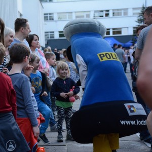 Wystawa przed budynkiem komendy. Policyjna maskotka Komisarz Błysk rozmawia z grupką dzieci.
