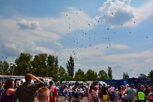 W niebo szybuje 100 niebieskich balonów wypuszczonych przez dzieci.