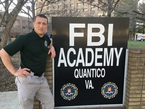 Uczestnik stojący koło tablicy z napisem &quot;FBI Academy Quantico VA.&quot;