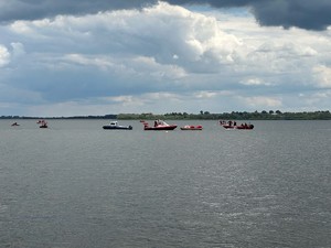 Na zdjęciu widać pływające łodzie wszystkich służb ratunkowych, takich jak straży pożarnej, wodnego ochotniczego pogotowia ratunkowego i policji. W tle chmury i drzewa.