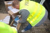 Policjant wyjmuje paczki papierosów z kartonu