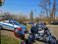 Na zdjęciu widocznych jest około 10 różnych motocykli stojących w sąsiedztwie radiowozu Wydziału Ruchu Drogowego KMP w Łodzi. W dalszym planie znajdują się jeszcze 4 cywilne pojazdy.