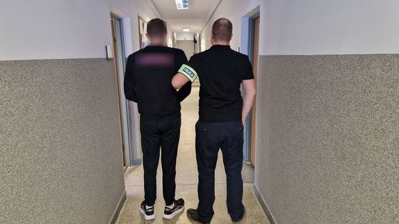 Nieumundurowany policjant stoi z zatrzymanym mężczyzną.