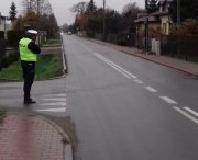 Umundurowany policjant stoi przy drodze i mierzy prędkość