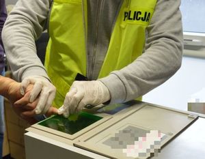 Policjant w białych rękawiczkach i żółtej kamizelce z napisem policja pobiera odciski palców.