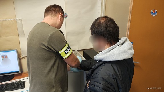 Technik kryminalistyki wykonuje daktyloskopię zatrzymanemu mężczyźnie.