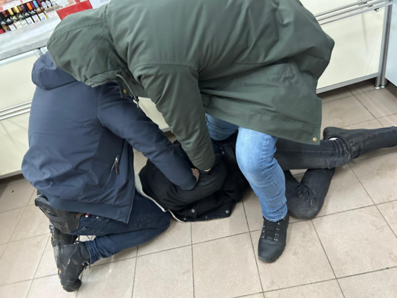 Policjanci operacyjnie zatrzymują mężczyznę, mężczyzna leży na posadzce twarzą do dołu, dwóch policjantów go przytrzymuje.