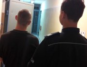 policjant w pomieszczeniu kpp Bełchatów prowadzi podejrzanego o kradzież białej broni