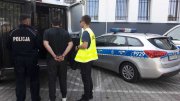 policjanci z zatrzymanym sprawcą kradzieży z włamaniem. prowadza go radiowozu policyjnego