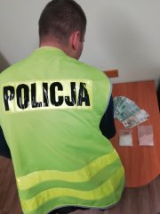 policjant w kamizelce przegląda środki odurzające i pieniądze