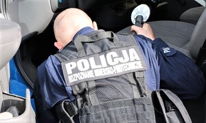 na zdjęciu policyjny  pirotechnik widoczny tyłem ,dokonuje sprawdzenia samochodu.