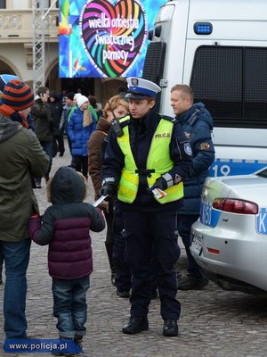 Policjant rozdający podczas Wielkiej Orkiestry Świątecznej Pomocy opaski odblaskowe.