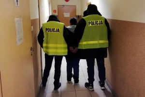 Policjanci prowadzą zatrzymaną kobietę.