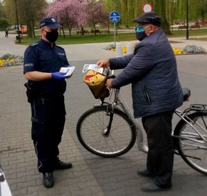Policjant daje maseczkę rowerzyście.