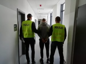 Dwaj policjanci prowadzą zatrzymanego korytarzem komisariatu.
