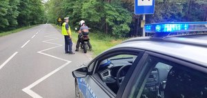 radiowóz i policjant kontrolujacy motocyklistę