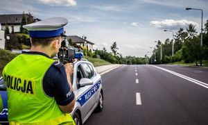 Radiowóz przy drodze i obok policjant ruchu drogowego mierzący prędkość.