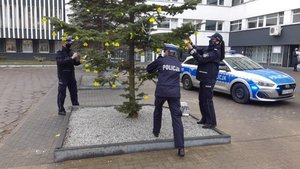 Dwie policjantki i policjant zakładają na choinkę odblaskowe elementy.