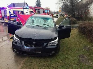 Rozbite BMW na poboczu drogi w tle pracują służby pogotowie strażacy i policja.