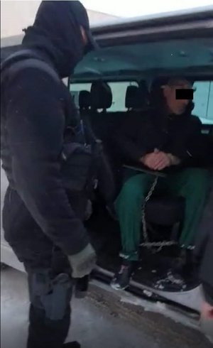 Zatrzymany skuty kajdankami siedzi w radiowozie, obok policjant.