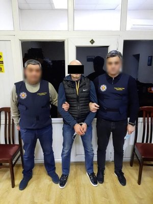 Dwaj policjanci gruzińscy w  środku zatrzymany mężczyzna, ma naniesiony czarny pasek na oczy,jest skuty w kajdanki.