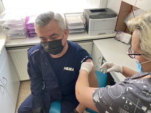 Zastępca Komendanta KWP w Łodzi  podczas szczepienia przeciw covid 19. Policjant w mundurze przebywa w gabinecie lekarskim.