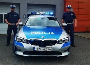 oznakowany radiowóz policji a obok dwaj umundurowani policjanci