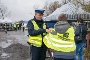 policjant zakłada kamizelke odblaskową pieszemu