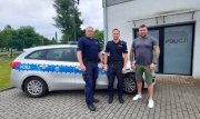 Policjanci stojący przed oznakowanym radiowozem.