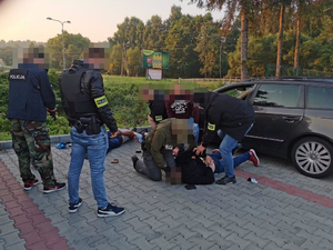 Skuty na ziemi mężczyzna obok policjanci po cywilnemu i dwa pojazdy.