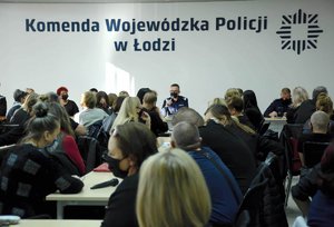 Napis na ścianie Komenda Wojewódzka Policji w Łodzi, za stołem prezydialnym siedzi dwóch mundurowych, jeden generał zabiera głos mówiąc przez mikrofon, sala wypełniona jest pracownikami cywilnymi.
