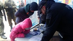 Na stoisku policyjnym dwaj policjanci w mundurach nachylają się na dziećmi.