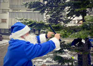 Policjanci z niebieskim Mikołajem wieszają odblaski na choince.