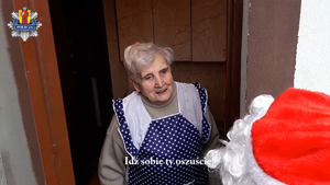 Starsza, siwa kobieta. Przed nią ktoś ubrany w czapkę św. Mikołaja. W tle logo policji województwa łódzkiego.