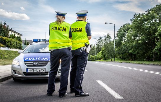 policjanci z drogówki stoją przy drodze, obok oznakowany radiowóz