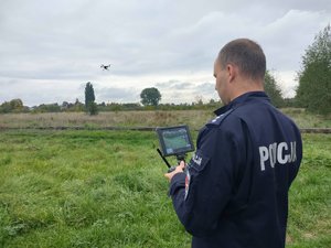 policjant w mundurze stoi na polu i operuje dronem