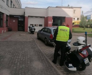 Stojące przed szpitalem dwa motocykle policyjne i umundurowany policjant.