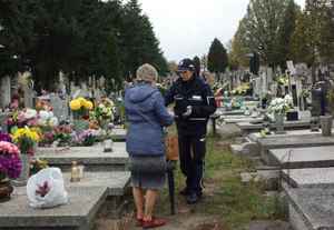 Policjantka w mundurze daje ulotkę pani sprzątającej na cmentarzu grób.