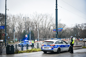 Ulica, na ulicy stoi radiowóz obok dwóch policjantów umundurowanych, na chodniku stoi radiowóz oznakowany obok stoi policjant.