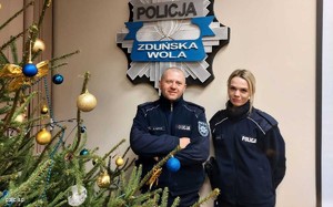 dwoje umundurowanych policjantów stoi przy choince, w tle widoczne logo zduńskowolskiej policji