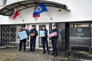 Czworo umundurowanych policjantów z paczkami w rękach stoi przed wejściem do komendy wojewódzkiej.